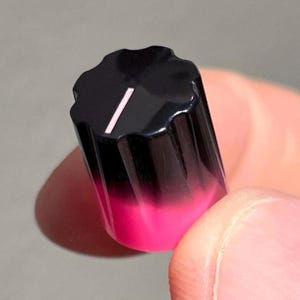 May include: A cylindrical control knob featuring a fluted exterior with a black top that transitions into a vibrant hot pink base. The top surface includes a single white indicator line, providing a clear visual reference for adjustment settings.