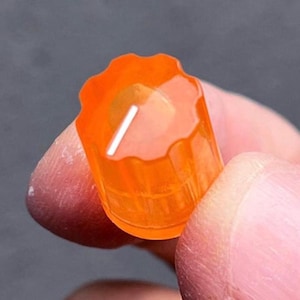 May include: A translucent orange cylindrical control knob featuring a scalloped, fluted edge and a single white indicator line on the top surface. The knob has a ridged exterior texture designed for grip and adjustment on electronic equipment.