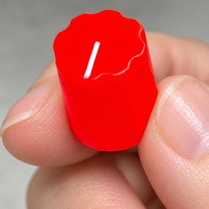 May include: A bright red cylindrical control knob featuring a scalloped, textured edge along the top circumference and a single white indicator line printed on the flat top surface for precise adjustment and visual alignment.