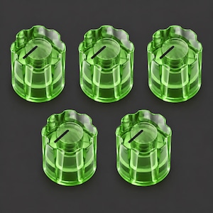 May include: A set of five translucent lime green knobs, each featuring a cylindrical body with a scalloped, fluted edge and a single black indicator line on the top surface, arranged in a pattern of three on top and two on the bottom.