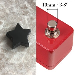 Pode incluir: Um pedal de metal vermelho com um botão preto em forma de estrela. O botão tem um diâmetro de 10 mm ou 3/8 de polegada.
