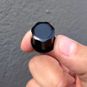 Peut inclure: Bouton noir en plastique avec un dessus rond et plat et une base à six côtés cannelée.