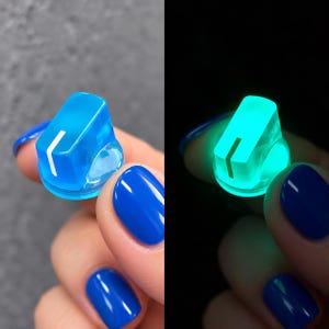 May include: A translucent blue control knob featuring a single white indicator line on the top surface. The knob is shown in two states: one in daylight appearing blue and one in darkness where the material emits a bright glowing cyan light.