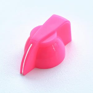 May include: A bright neon pink control knob with a smooth, rounded base and a prominent pointer arm extending from the center. A thin, vertical white line is etched into the side of the pointer arm to indicate the current setting position.
