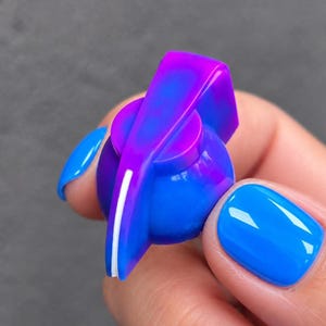 以下が含まれることがあります： 青と紫の鮮やかなグラデーションが特徴の丸いコントロールノブ。ノブには隆起したポインターアームがあり、側面には細い白い線が入っています。電子機器やオーディオ機器の精密な調整用に設計された部品です。