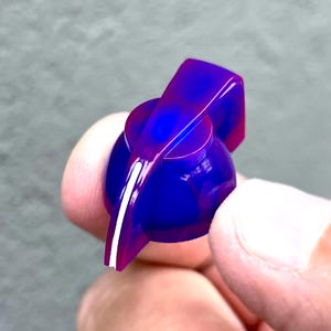 Op de afbeelding: Een paarse en blauwe gitaarknop met een witte lijn in het midden. De knop is gemaakt van plastic en heeft een afgeronde vorm.