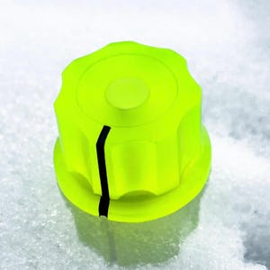 May include: A bright neon yellow control knob featuring a circular top with a raised center and a fluted, scalloped edge. A single vertical black indicator line runs from the top edge down to the base of the knob, providing a clear visual reference.