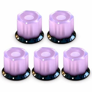 Puede incluir: Un juego de cinco perillas cilíndricas con un acabado translúcido de color morado claro y un diseño lateral estriado y festoneado. Cada perilla presenta una hendidura circular en la parte superior y una base oscura reflectante con un pequeño punto blanco.