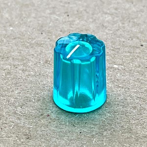 Könnte beinhalten: Ein knallblauer Kunststoffknopf mit geriffeltem Design. Der Knopf hat ein kleines Loch in der Mitte.