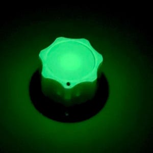 以下が含まれることがあります： 星型の上面と円形の基部を持つ、光る緑色のノブ。暗い背景の中で明るく均一な光を放ち、コントロールまたはインジケーターを示唆しています。