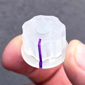 May include: A clear, translucent plastic control knob with a circular, fluted edge design. The knob features a single, vertical purple stripe running down the side, serving as a visual indicator for alignment and adjustment settings.