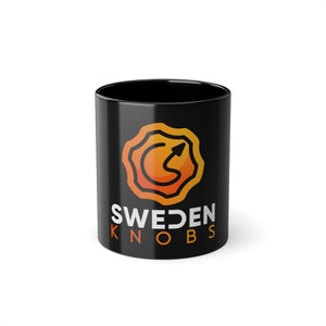 Puede incluir: Taza de cerámica negra con un logotipo blanco que dice "SWEDEN KNOBS" y un gráfico de una flecha naranja y amarilla en un círculo.