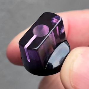 May include: A translucent dark purple control knob with a smooth, glossy finish. The top surface features a circular indentation and a single straight line indicator filled with a lighter purple color, designed for audio equipment adjustment.