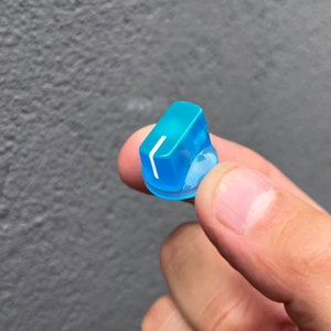 Puede incluir: Un mando de pl&aacute;stico azul claro con una l&iacute;nea blanca. El mando est&aacute; siendo sujetado por una mano.