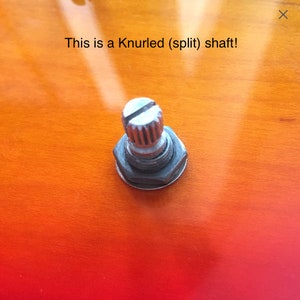 Puede incluir: Primer plano de un eje acanalado (dividido) plateado en una guitarra. El eje est&aacute; unido a una perilla negra.