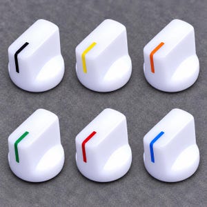 May include: A set of six white plastic control knobs, each featuring a single vertical indicator line. The indicator lines are colored black, yellow, orange, green, red, and blue, respectively, providing a clear visual distinction for each knob.