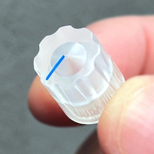 May include: A clear, cylindrical control knob featuring a scalloped top edge and a vertical ribbed side texture. A single, thin, bright blue indicator line is printed on the top surface, extending from the center toward the outer edge.