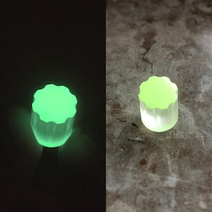 Puede incluir: Un pomo verde que brilla en la oscuridad con un diseño de estrella. El pomo está hecho de plástico y tiene una superficie lisa y redondeada.