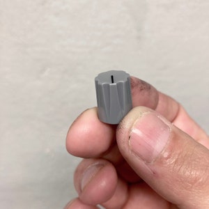 May include: A grey plastic knob with a single vertical line on the top.