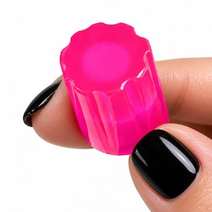 May include: A small, translucent, neon pink cylindrical object with a fluted, scalloped edge along the top rim. The item features a smooth, semi-transparent finish and a distinct vertical ribbed texture around its outer circumference.