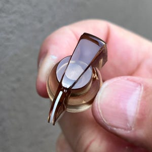 以下が含まれることがあります： 半透明の茶色のプラスチック製コントロールノブで、円形のベースと先細りのポインターが付いています。ポインターの上端には細い白い垂直線があり、ノブの中央には円形のすりガラス状の半透明のインレイが施されています。