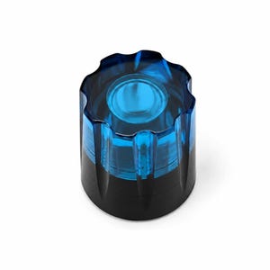 Pode incluir: Um botão cilíndrico com uma secção superior azul translúcida com uma borda recortada e estriada e uma base preta sólida. O design inclui uma reentrância circular no centro da superfície superior, proporcionando um contraste claro entre a parte superior azul vibrante e o componente inferior preto opaco.