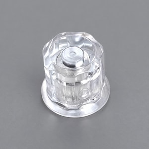 Peut inclure: Une poignée de robinet en acrylique transparent à facettes avec une base circulaire et un insert central en métal argenté. Le bouton présente un design extérieur octogonal à plusieurs côtés avec des stries verticales pour la prise.