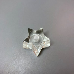 Pode incluir: Um porta-velas de vidro transparente em forma de estrela com uma pequena depressão redonda no centro.