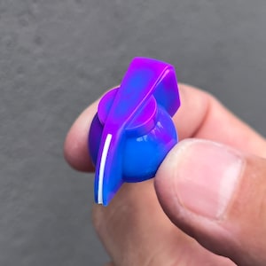 Könnte beinhalten: Ein lila und blauer Gitarrenknopf mit einer weißen Linie in der Mitte.