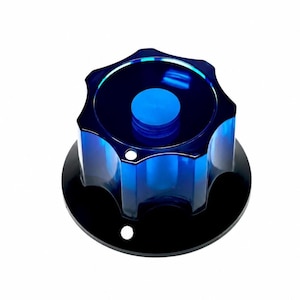 May include: A translucent blue, star-shaped knob with six rounded points, featuring a smooth, glossy finish. The knob is mounted on a solid black circular base plate that includes two small, circular mounting holes positioned near the outer edge.