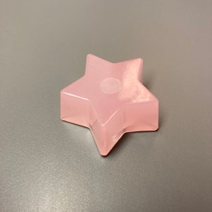 Op de afbeelding: Een roze stervormig papieren gewicht van hars met een wit swirl-ontwerp.