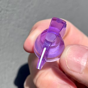 Op de afbeelding: Een paarse plastic knop met een witte lijn in het midden. De knop is ontworpen om te worden gedraaid om een instelling aan te passen.