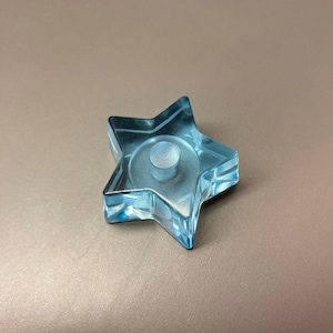 Puede incluir: Un portavelas de vidrio en forma de estrella de color azul claro con una hendidura redonda en el centro.