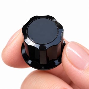 May include: A glossy black control knob featuring a circular top surface and a fluted, scalloped side profile with vertical ridges. The component has a smooth, reflective finish and a wide, flat base, designed for adjustment on electronic equipment.