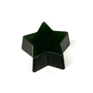 May include: A dark green, star-shaped object with a glossy finish. The five-pointed star has a slightly rounded shape and is set against a white background. The object appears to be made of a solid material.