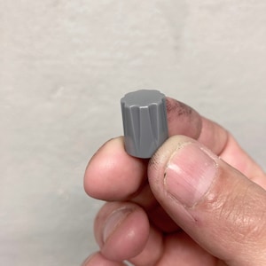 Puede incluir: Un pomo de plástico gris con un diseño acanalado. El pomo tiene un diámetro de aproximadamente 2,5 cm.