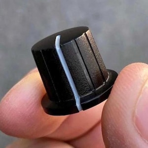 May include: A black cylindrical control knob featuring a textured, ribbed exterior surface and a single vertical white indicator line running from the top edge down the side, designed for adjusting electronic equipment settings.