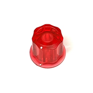 May include: A transparent red knob with a circular base and a ridged, hexagonal top. The knob has a hole in the centre and two small holes on the base. The object is likely a control knob for an electronic device.