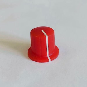 Könnte beinhalten: Ein leuchtend roter Drehknopf mit einem weißen Indikatorstrich. Der Knopf hat eine zylindrische Oberseite und eine kreisförmige Basis. Dieses elektronische Bauteil wird wahrscheinlich zum Einstellen von Einstellungen an Audiogeräten oder anderen Geräten verwendet.
