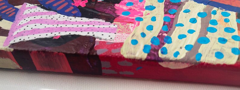May include: Close-up of a colorful abstract painting with pink, blue, white, and brown paint. The painting has a textured surface and a variety of patterns, including stripes, dots, and swirls.