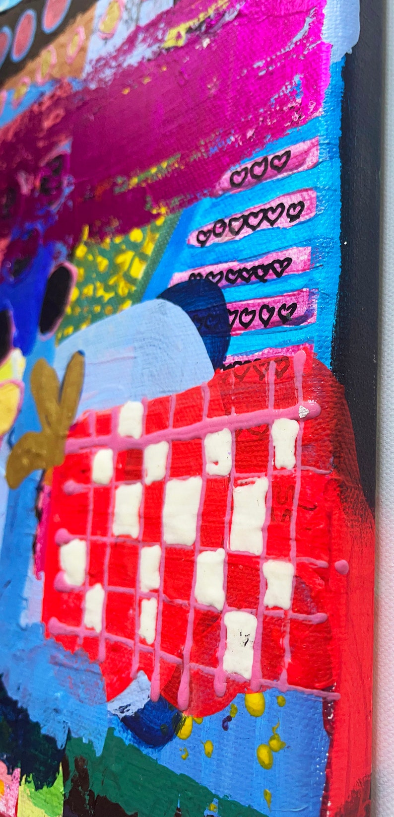 Pode incluir: Pintura abstrata com um padr&atilde;o xadrez vermelho e branco, listras rosa e azuis e cora&ccedil;&otilde;es pretos. A pintura est&aacute; em tela e tem uma superf&iacute;cie texturizada.
