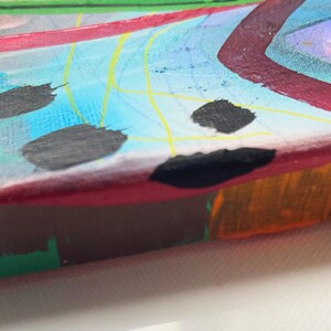 May include: Abstract painting on canvas with a colourful, geometric design. The painting features a mix of bright colours, including red, blue, green, yellow, and orange. The edges of the canvas are visible, showing the raw canvas material.