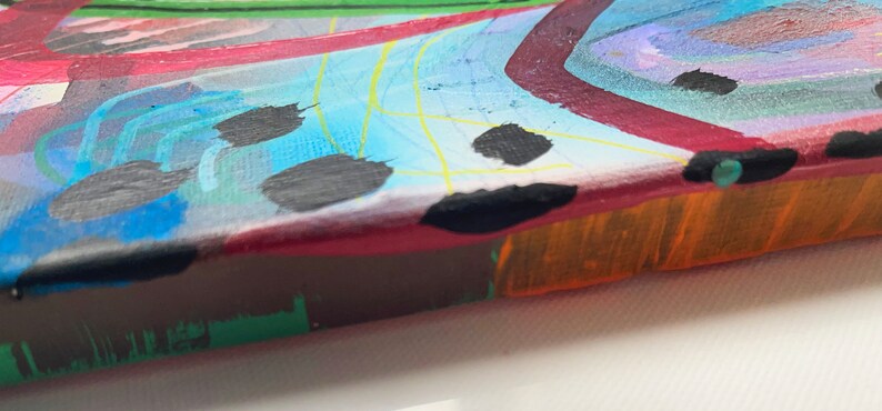 May include: Abstract painting on canvas with a colourful, geometric design. The painting features a mix of bright colours, including red, blue, green, yellow, and orange. The edges of the canvas are visible, showing the raw canvas material.
