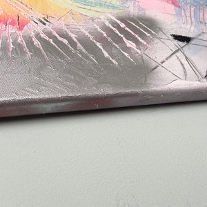 May include: Close-up of the edge of a silver canvas painting with abstract shapes and colors. The canvas is textured and has a pink, white, and black color scheme.