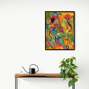 May include: Abstract painting in a black frame with a yellow background and colorful shapes, lines, and swirls. The painting is hanging on a white wall above a wooden table with a black metal frame.