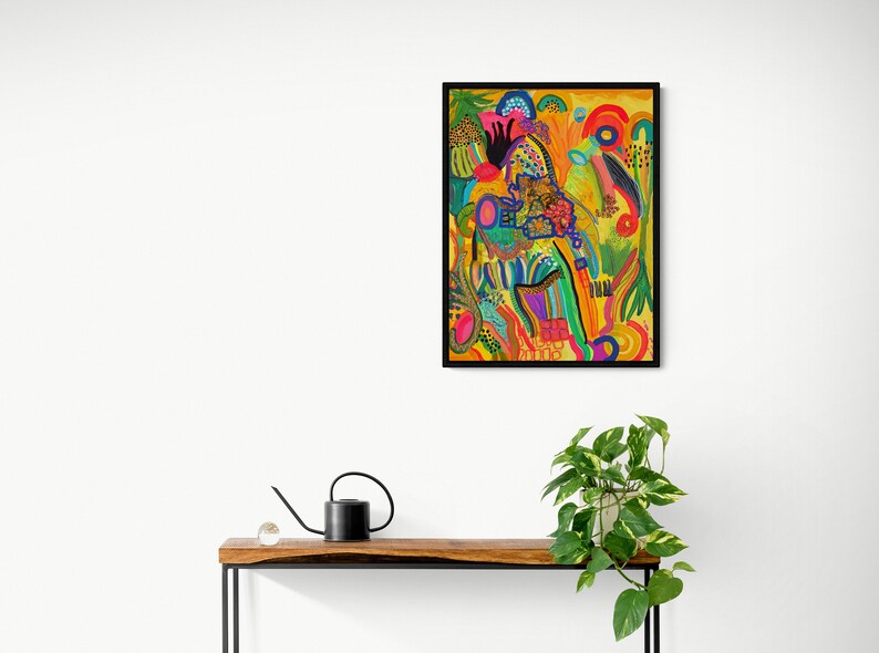 May include: Abstract painting in a black frame with a yellow background and colorful shapes, lines, and swirls. The painting is hanging on a white wall above a wooden table with a black metal frame.