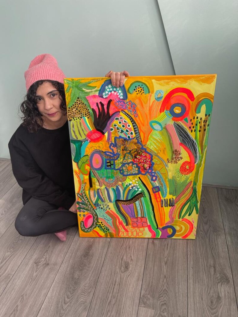 May include: A colorful abstract painting with a yellow background and bright green, pink, blue, and orange shapes. The painting is framed and has a textured surface.