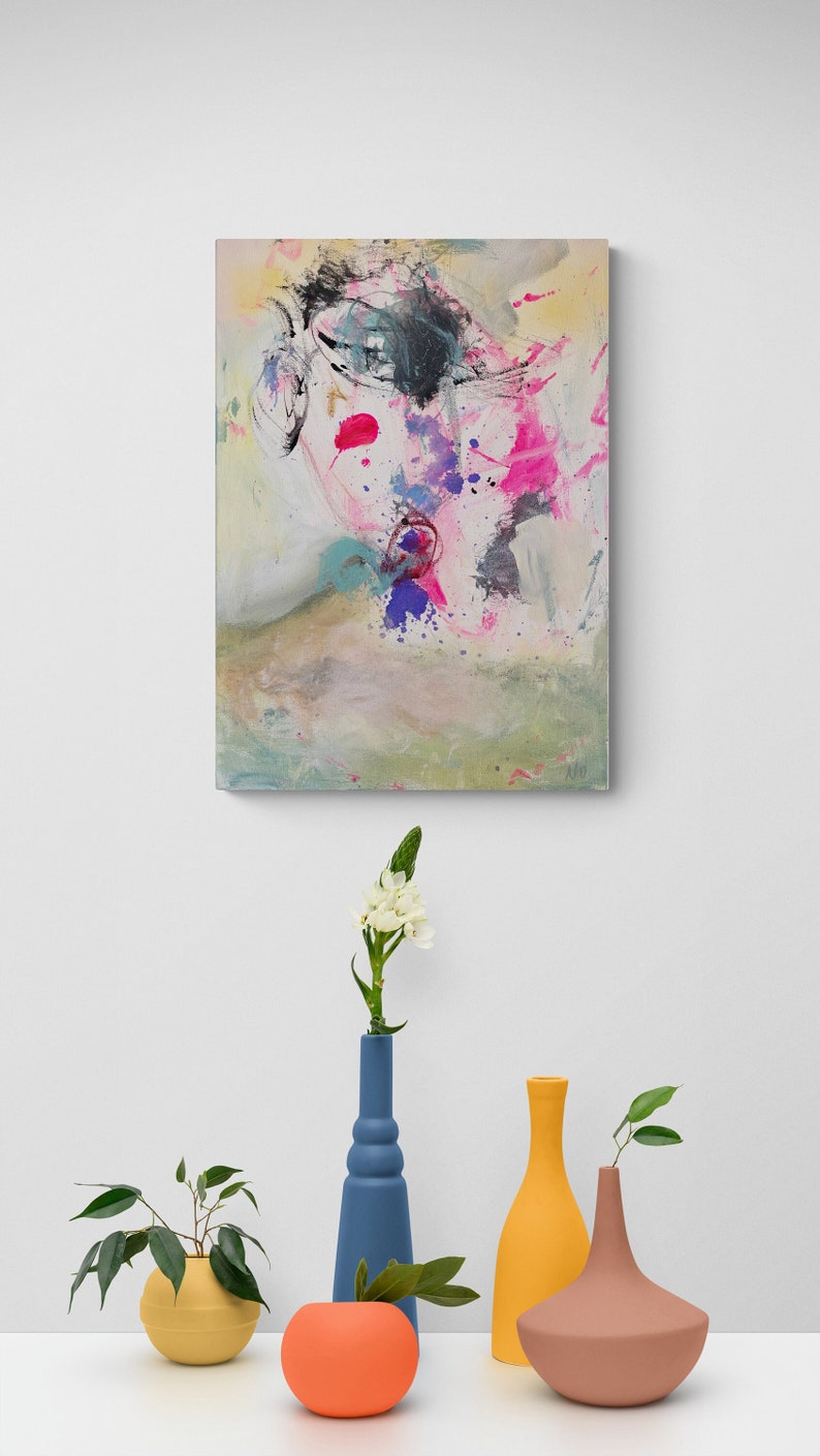 Puede incluir: Una pintura abstracta colorida con salpicaduras de rosa, azul y amarillo cuelga de una pared blanca sobre una mesa con cuatro jarrones. Los jarrones son azules, amarillos, marrones y naranjas. Una peque&ntilde;a planta est&aacute; en el jarr&oacute;n amarillo.