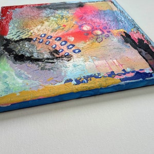 May include: Abstract painting on canvas with a textured surface. The painting features a mix of colors, including red, pink, blue, yellow, and black. The edges of the canvas are painted blue and gold.