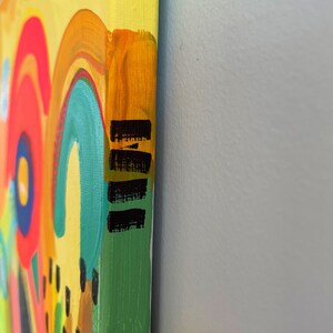 May include: Close-up of the side of a canvas painting with a colorful abstract design. The edges of the canvas are painted yellow, orange, green, and black.